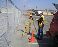 A surveyor using a tripod tool in front of a chain link fence