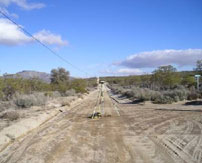 Tripod survey tool in the middle of a wide dirt road lined with brushes and trees